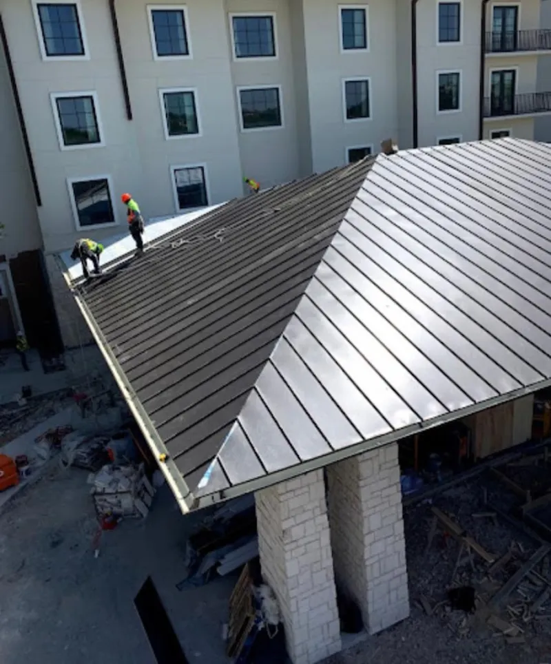 Crew installing standing seam metal roof panels on a commercial project in Irving